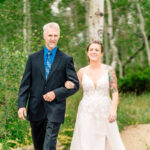 A bride and her father walking down a path in the woods.