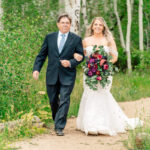 A bride and her father walking down a path in the woods.