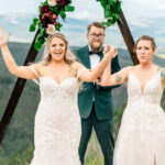 A bride and groom stand in front of a wedding arch in the mountains.
