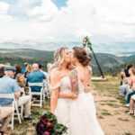 Two brides kissing at their wedding ceremony in the mountains.
