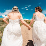 Two brides walking down a dirt road holding hands.