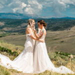 Two brides standing on a hillside with mountains in the background.