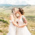 Two brides kissing in the mountains on their wedding day.