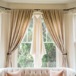 A wedding dress hangs on a couch in front of a window.