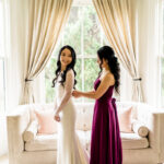Two brides getting ready in a room with large windows.