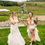 Two brides laughing in the grass at their wedding.
