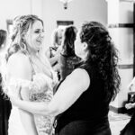 A bride dances with her bridesmaids in a black and white photo.