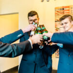 A group of groomsmen toasting with a bottle of beer.