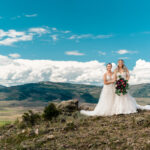 Two brides standing on top of a hill with mountains in the background.