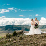 Two brides standing on top of a hill with mountains in the background.