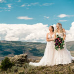 Two brides standing on top of a mountain with mountains in the background.