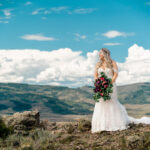 A bride standing on top of a mountain with mountains in the background.