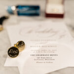 A wedding invitation with a watch and cufflinks on a table.