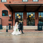 A bride and groom walking in front of a brick building.