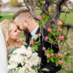 A bride and groom kissing under an apple tree.
