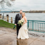 A bride and groom standing in front of a bridge in the rain.