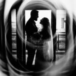A black and white photo of a bride and groom standing in front of a circular window.