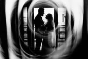 A black and white photo of a bride and groom standing in front of a circular window.