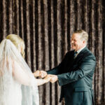 A bride and groom shake hands in a hotel room.