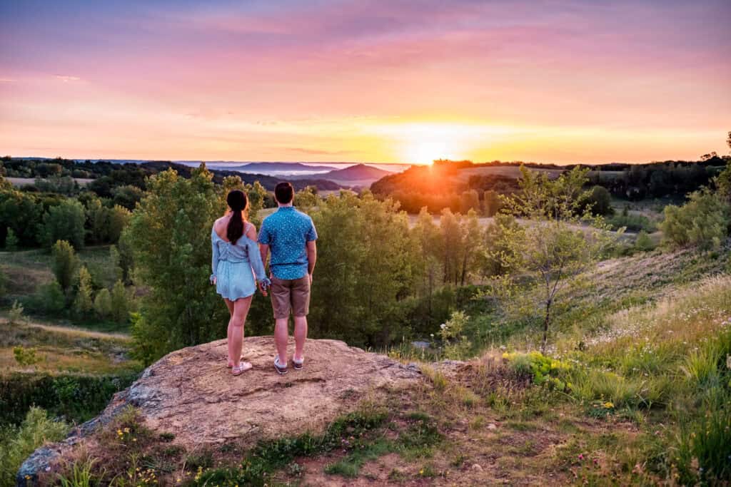 Young couple standing on top of a hill at sunset.