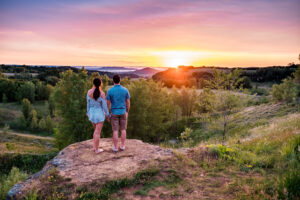 Young couple standing on top of a hill at sunset.