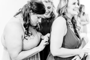 Two bridesmaids helping each other with their wedding rings.
