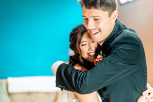 A bride and groom hugging in front of a blue wall.