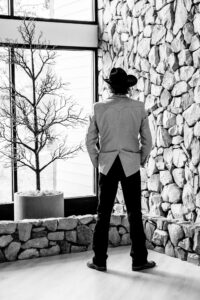 A man in a cowboy hat standing in front of a stone wall.