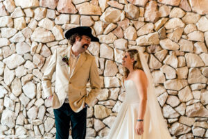 A bride and groom standing in front of a stone wall.