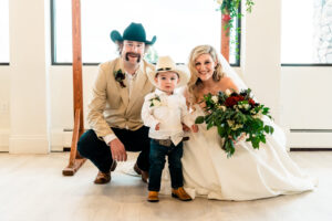 A bride and groom in cowboy hats pose for a photo with their son.