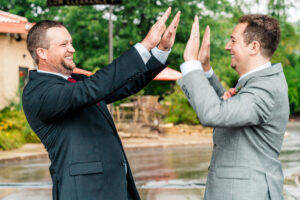 Two grooms giving each other high fives in the rain.