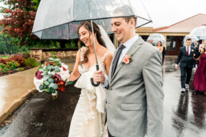 A bride and groom holding umbrellas in the rain.