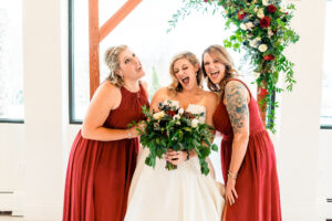 Three bridesmaids laughing in front of a wedding arch.