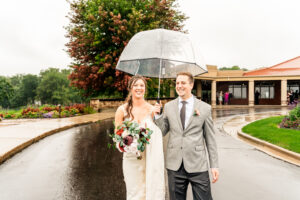 A bride and groom holding an umbrella in the rain.