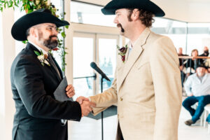 Two men in cowboy hats shaking hands at a wedding.
