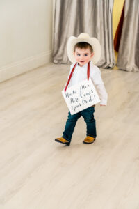 A baby boy in a cowboy hat holding a sign.