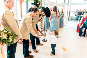 A little boy is holding a cowboy hat during a wedding ceremony.