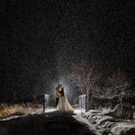 A bride standing on a bridge in the snow at night.