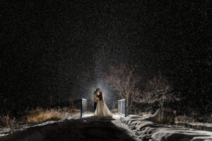 A bride standing on a bridge in the snow at night.