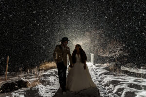 A bride and groom standing in the snow at night.