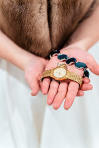 A woman's hands holding a watch and necklace.