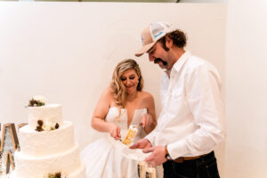 A bride and groom cutting into a white wedding cake.
