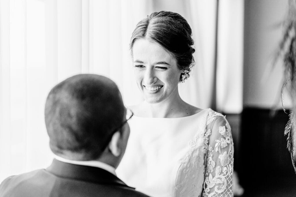 A woman in a white dress smiles at a person facing her. The image is in black and white.