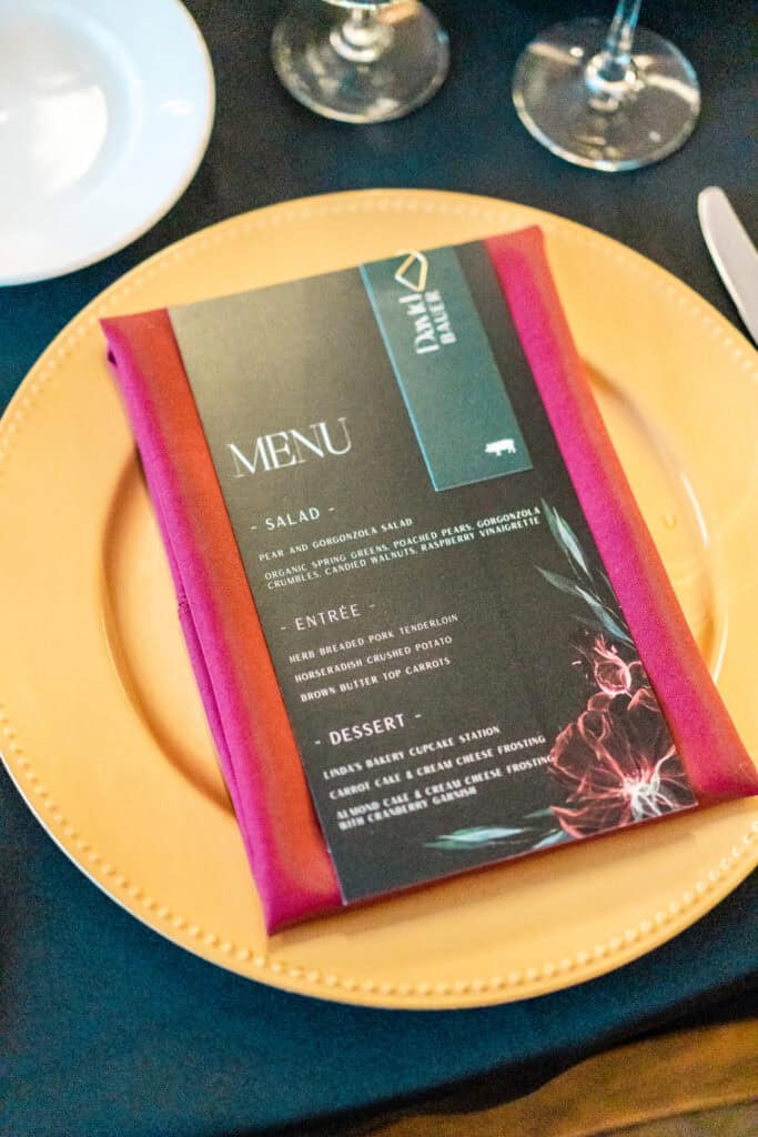 Dinner menu on a yellow plate, featuring options for salad, entree, and dessert. The menu is wrapped in a red napkin, with a black and gold design, set on a black tablecloth.