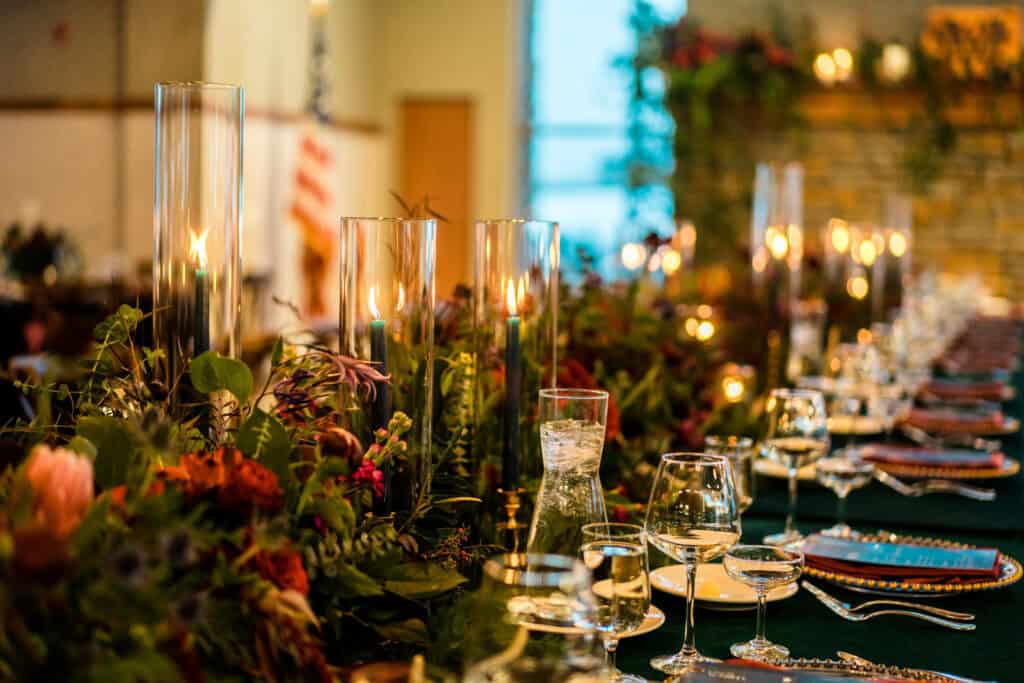A long dinner table is elegantly set with tall candleholders, glassware, and floral arrangements, ready for a formal event.