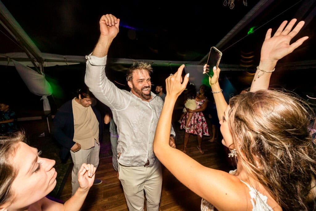People are dancing and raising their arms at a lively event or celebration under a tent.