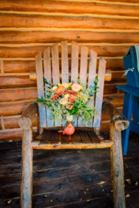 A rustic wooden chair with a bouquet of flowers and greenery placed on the seat and a small decorative gourd on the wooden floor in front of it.