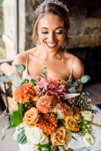 A woman in a white dress holds a vibrant bouquet of flowers and smiles while looking down, beautifully captured by a Vail Wedding Photographer.