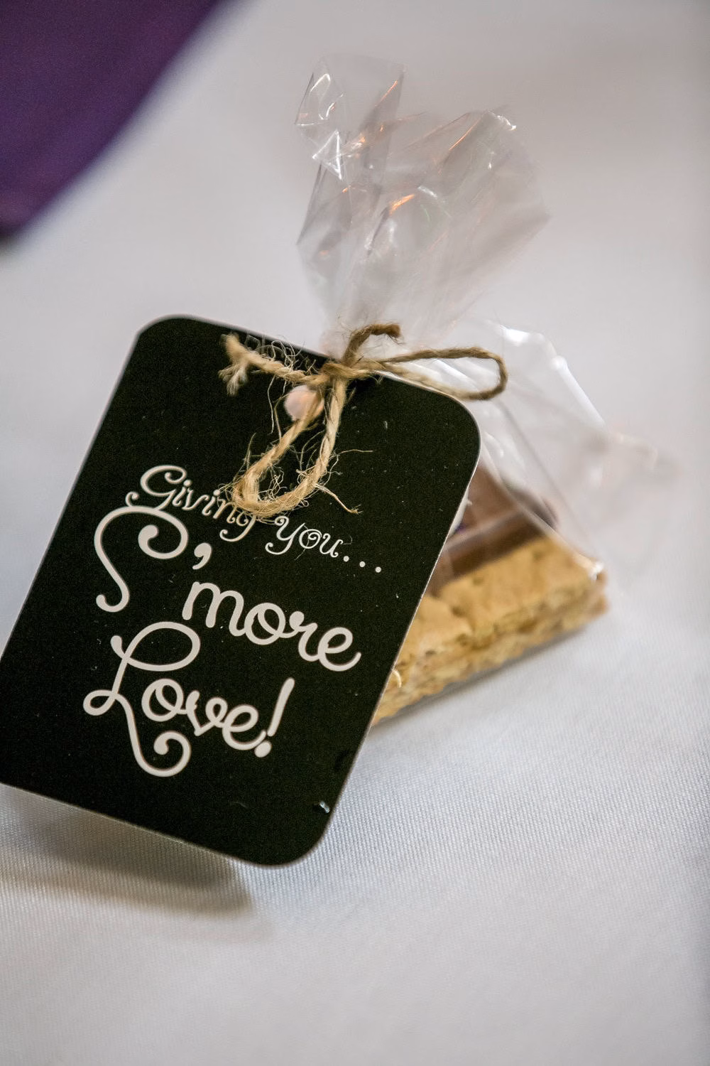 A wrapped s'mores kit with a tag reading "Giving you... S'more Love!" tied with twine, placed on a white surface.