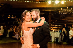 A bride and groom dance together at their wedding reception in a warmly lit venue, with guests seated at tables in the background, captured beautifully by a Vail Wedding Photographer.